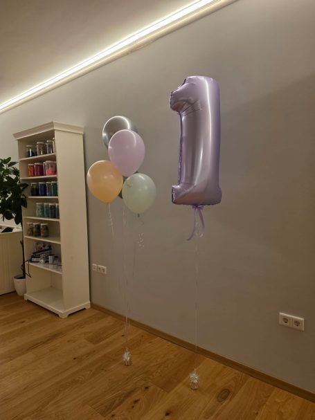 Lila Luftballon in Form der Zahl 1 und mehrere bunte Ballons in einem Raum.