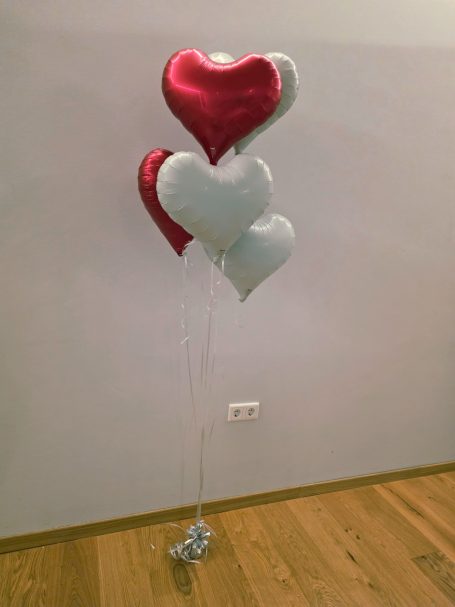 Drei herzförmige Luftballons in Rot und Silber, an Schnüren befestigt.